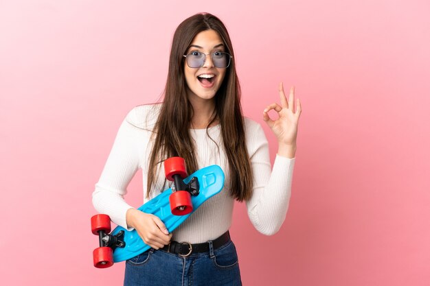 Teenager Brazilian girl over isolated background with a skate and doing OK sign