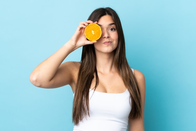 Teenager Brazilian girl over isolated blue wall holding an orange