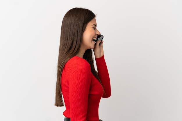 Teenager Brazilian girl using mobile phone over isolated white background laughing in lateral position