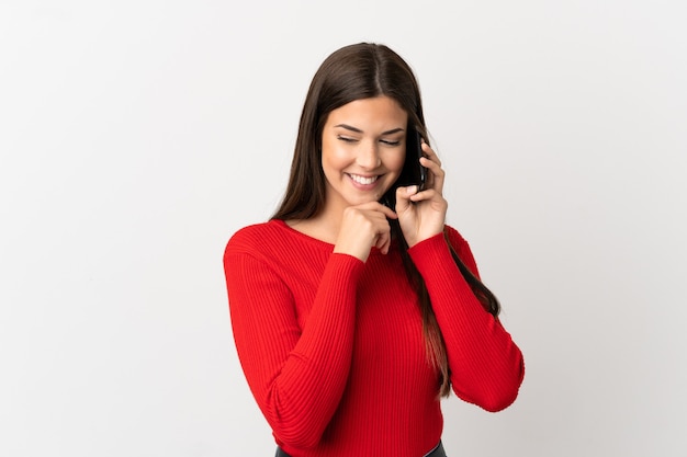 Foto ragazza brasiliana dell'adolescente che per mezzo del telefono cellulare sopra fondo bianco isolato che osserva al lato e che sorride