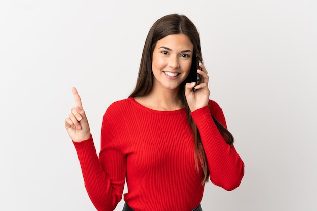 Teenager Brazilian girl using mobile phone over isolated white background pointing up a great idea