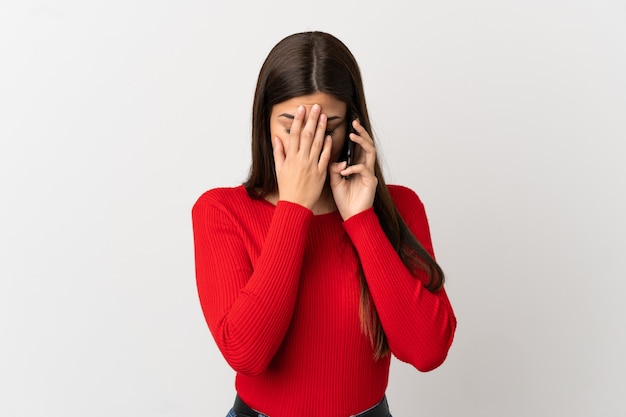 Teenager Brazilian girl using mobile phone over isolated white background with tired and sick expression