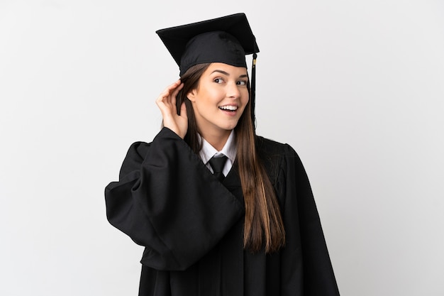 Teenager Brazilian university graduate over isolated white background listening to something by putting hand on the ear