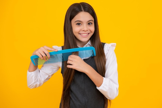 Teenager brushing combing hair with big comb on yellow isolated studio background teen girl with hairbrush kids hairstyle