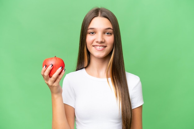 孤立した背景の上にリンゴを保持しているティーンエイジャーの白人の女の子は、たくさんの笑顔を浮かべています