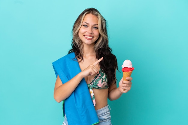 Teenager caucasian girl holding ice cream and towel isolated on blue background pointing to the side to present a product