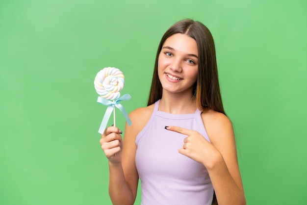 Teenager caucasian girl holding a lollipop over isolated background and pointing it