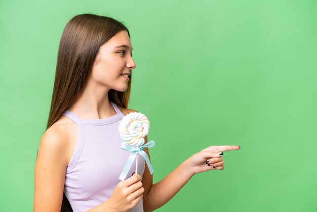 Teenager caucasian girl holding a lollipop over isolated background pointing to the side to present a product