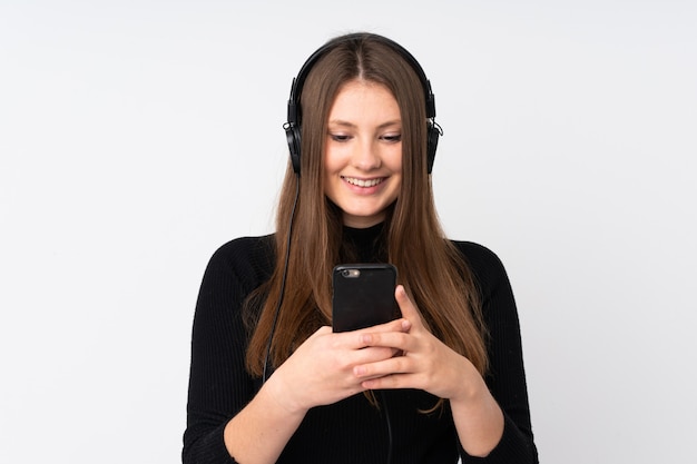 Teenager caucasian girl isolated on white listening music and looking to mobile