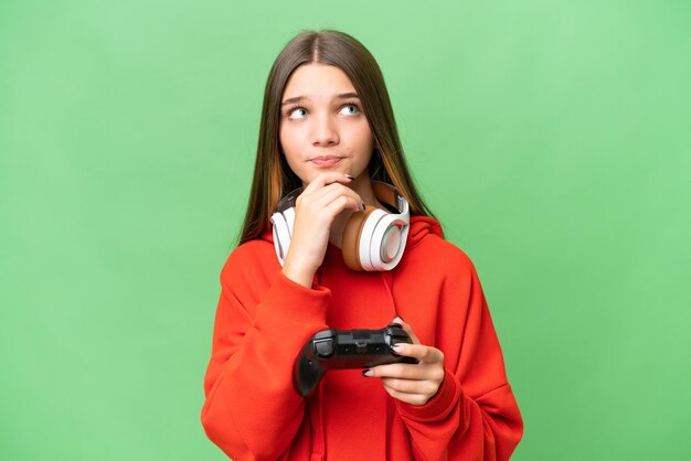 Teenager caucasian girl playing with a video game controller over isolated background and looking up