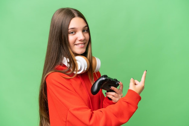 Teenager caucasian girl playing with a video game controller over isolated background pointing back