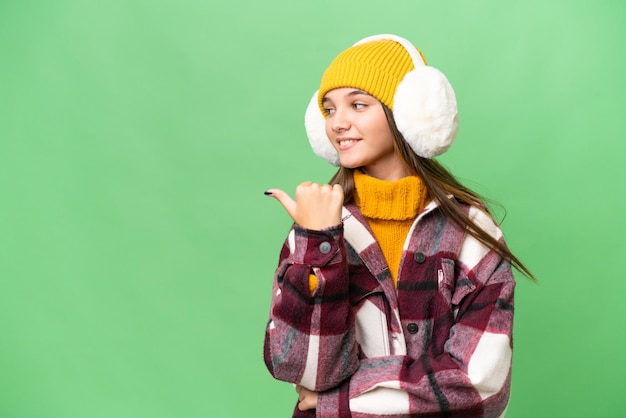 Teenager caucasian girl wearing winter muffs over isolated background pointing to the side to present a product