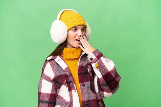 Teenager caucasian girl wearing winter muffs over isolated background yawning and covering wide open mouth with hand