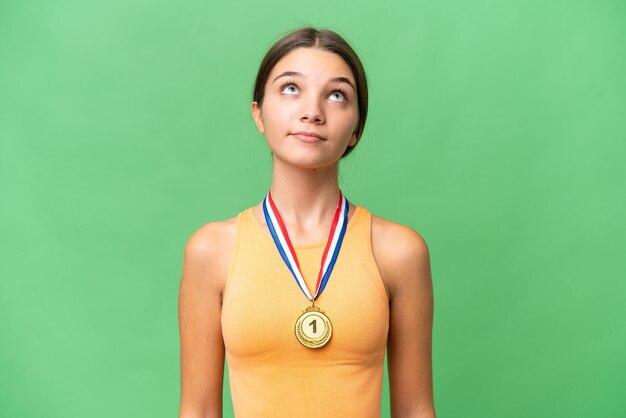 Teenager caucasian girl with medals over isolated background and looking up