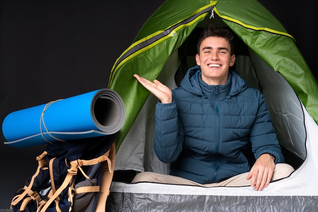 Foto uomo caucasico dell'adolescente dentro una tenda verde di campeggio isolata sul nero