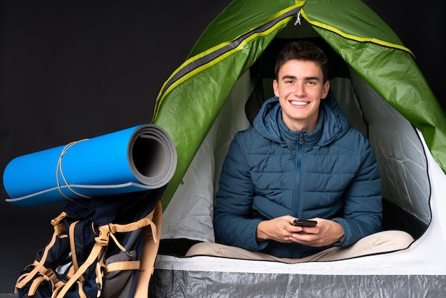 Foto uomo caucasico dell'adolescente dentro una tenda verde di campeggio isolata sul nero