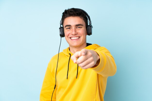 Teenager caucasian man isolated on purple listening music and pointing to the front