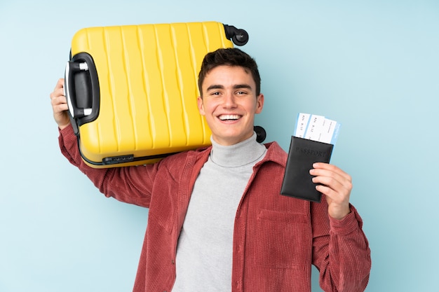 Uomo caucasico dell'adolescente sulla parete viola in vacanza con la valigia e il passaporto