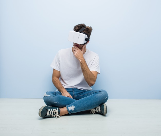 Teenager caucasian man using a virtual reality glasses sitting floor