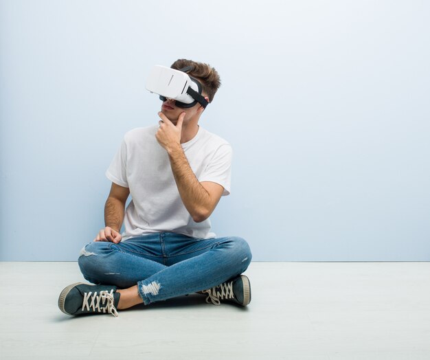 Teenager caucasian man using a virtual reality glasses sitting on the floor