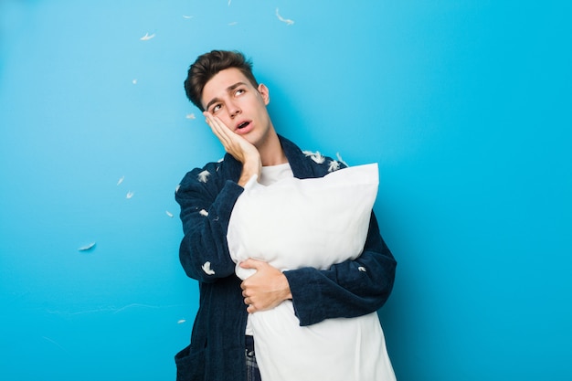 Teenager caucasian tired man holding a pillow