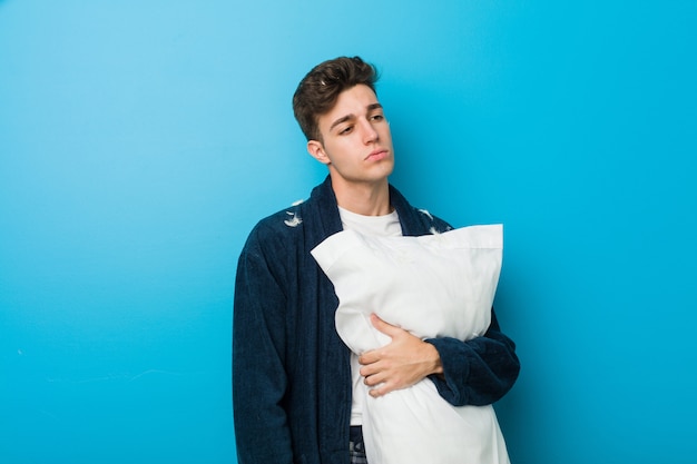 Teenager caucasian tired man holding a pillow