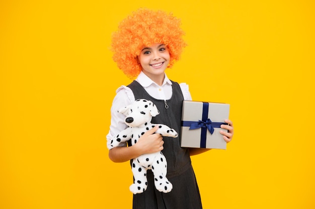 Teenager child in funny wig holding gift box on yellow isolated\
background gift for kids birthday christmas or new year present box\
funny child clown in wig and gift