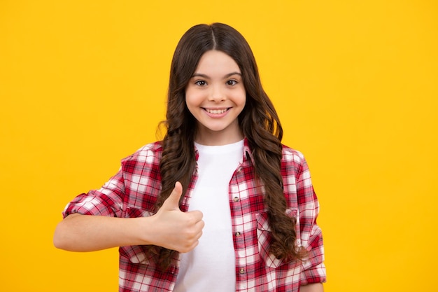 Teenager child girl 12 13 14 year old doing thumbs up gesture cheerful teenager girl showing thumbs up sign isolated on yellow background happy teenager positive and smiling emotions