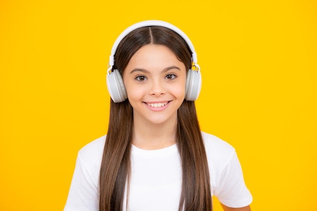 Teenager child girl in headphones listening music wearing stylish casual outfit isolated over yellow background happy teenager portrait smiling girl