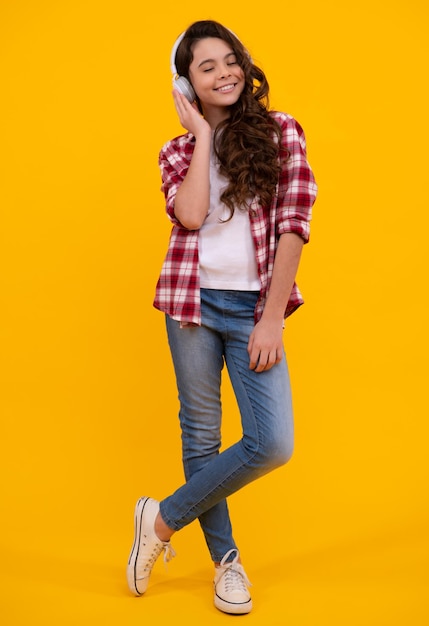 Teenager child girl in headphones listening music wearing stylish casual outfit isolated over yellow background Happy teenager with earphones positive and smiling emotions of teen girl