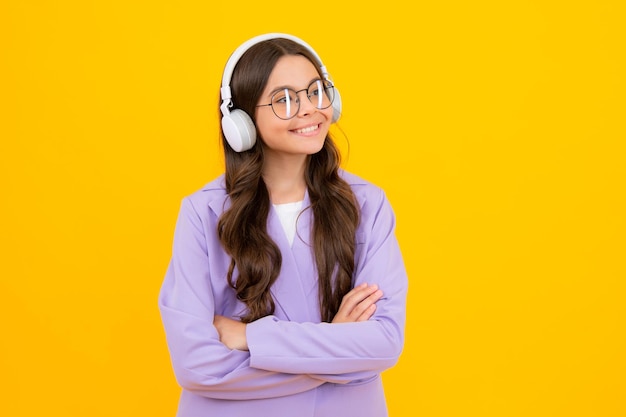 黄色の背景に分離されたスタイリッシュなカジュアルな服装を着て音楽を聴くヘッドフォンで 10 代の子供の女の子