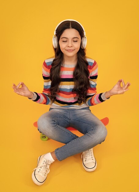 Teenager child girl in headphones listening music wearing stylish casual outfit isolated over yellow background