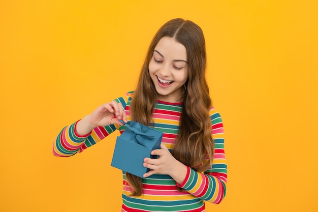 Teenager child girl holding present box isolated over yellow studio background present greeting and gifting concept birthday holiday concept
