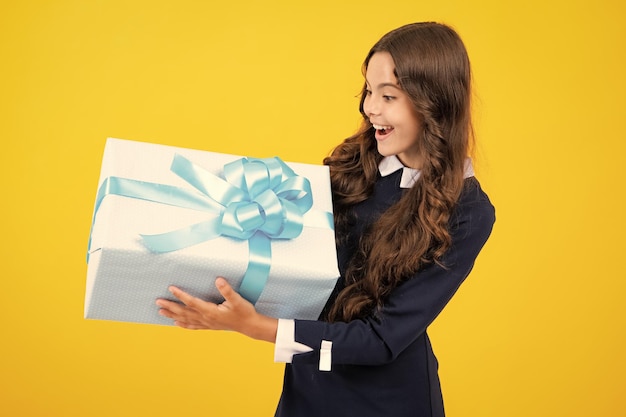 Teenager child girl holding present box isolated over yellow studio background Present greeting and gifting concept Birthday holiday concept