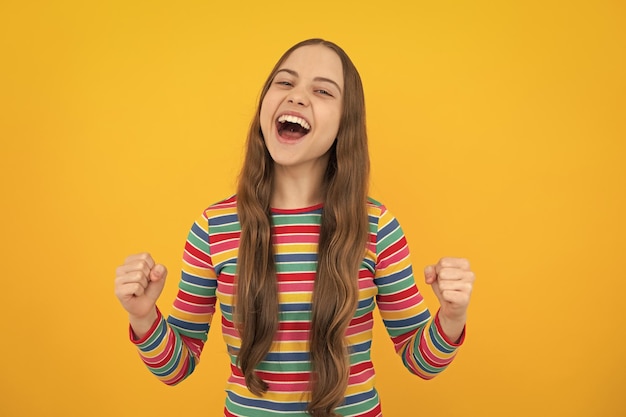 Teenager child girl rejoicing say yes looking happy and celebrating victory champion gesture fist pump on yellow background excited face cheerful emotions of teenager girl