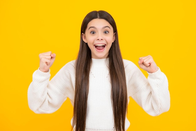 Teenager child girl rejoicing say yes looking happy and celebrating victory champion gesture fist pump on yellow background