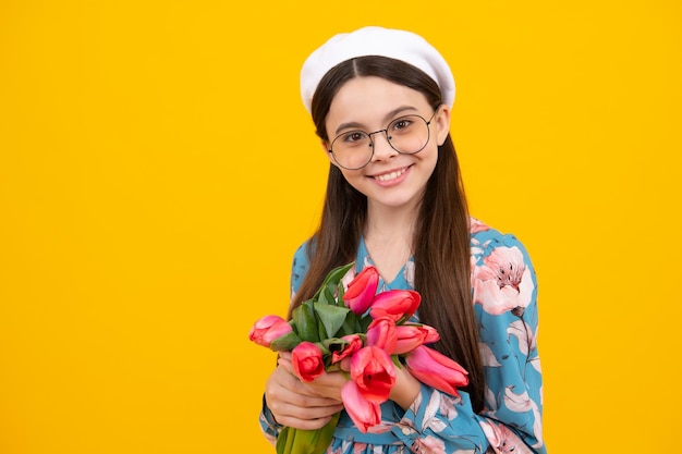 Teenager child girl with bouquet of tulips on yellow studio background Girl enjoying flowers