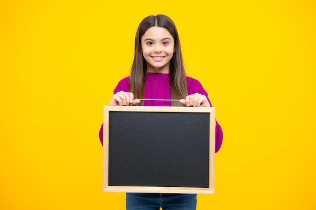 Teenager child holding blank chalkboard for message Isolated on a yellow background Empty text blackboard copy space mock up