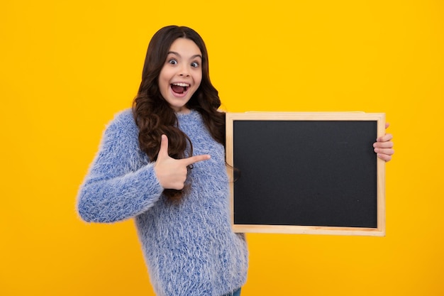 Teenager child holding blank chalkboard for message isolated on a yellow background empty text