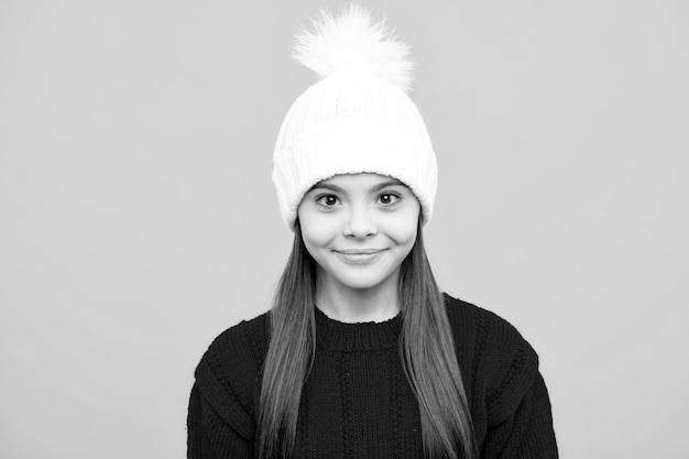 Teenager child in winter knitted hat and sweater having over yellow background