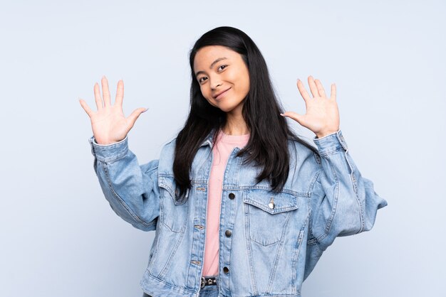 Teenager Chinese woman on blue wall counting ten with fingers