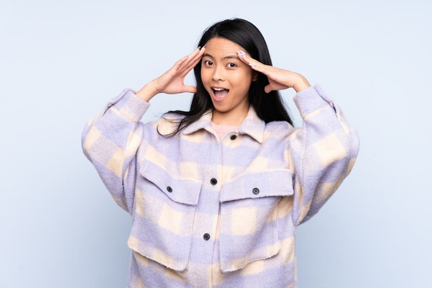 Teenager Chinese woman on blue wall with surprised expression