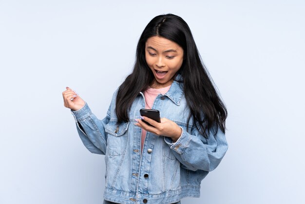 Teenager Chinese woman isolated on blue background surprised and sending a message