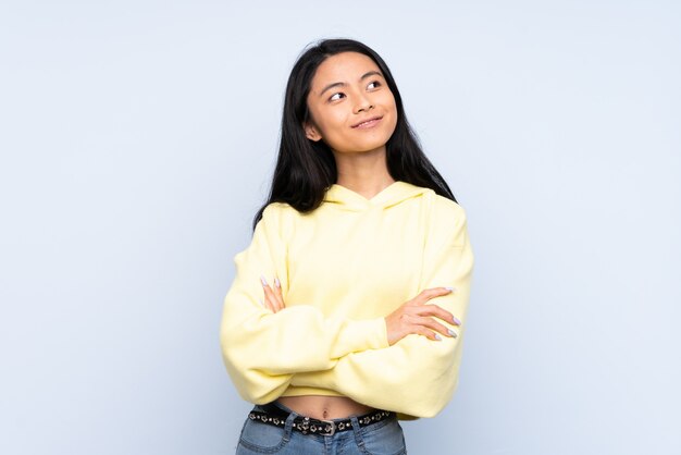 Teenager Chinese woman isolated on blue wall looking up while smiling