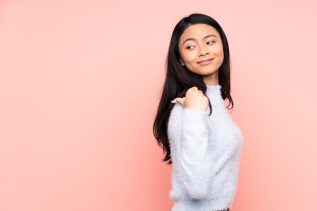 Teenager Chinese woman isolated on pink pointing to the side to present a product