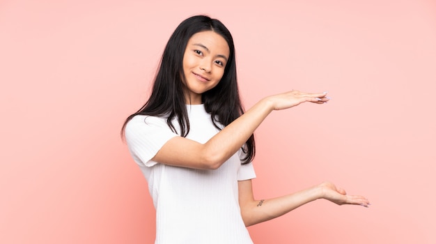 Teenager Chinese woman isolated on pink wall holding copyspace to insert an ad