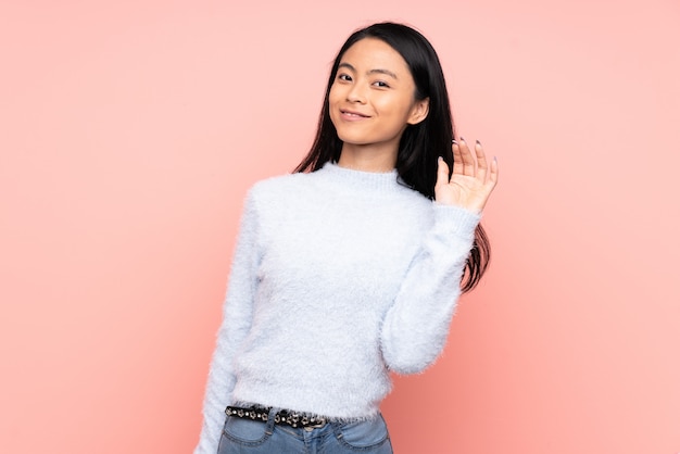 Teenager Chinese woman on pink wall saluting with hand with happy expression