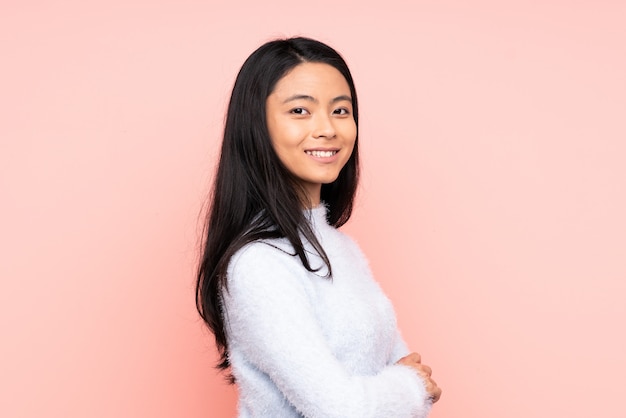 Teenager Chinese woman on pink wall with arms crossed and happy