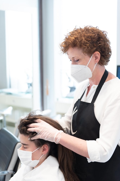 A teenager client wearing a face mask getting a hair massage in a beauty salon