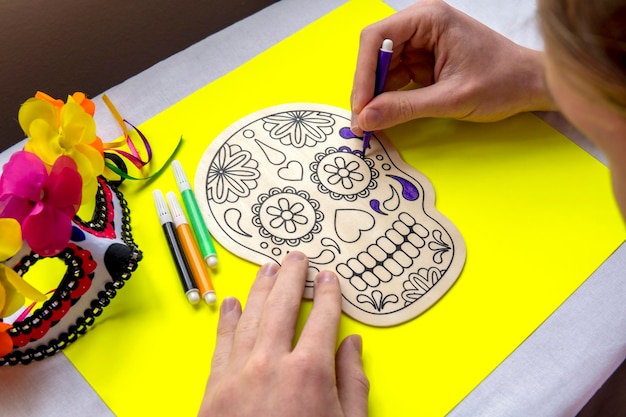 Teenager coloring with felt-tip pens wooden skull on yellow background. Day of the dead concept